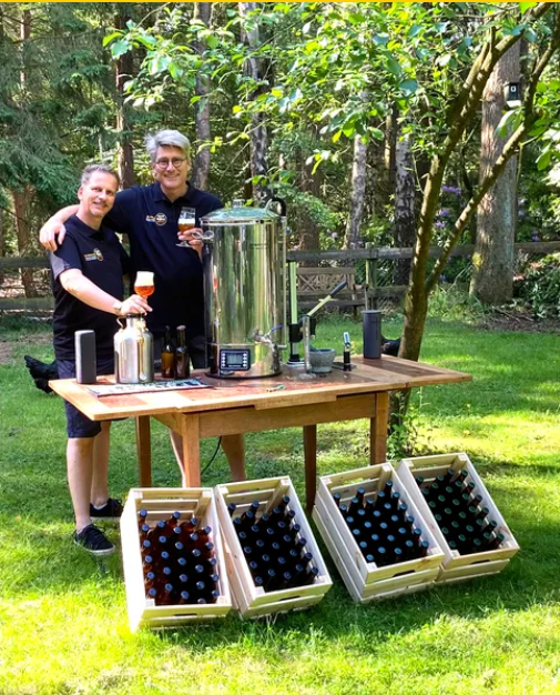 Peter en Piér van PopHop met de arm om elkaar heen bij hun brouwketel in de tuin, met kratten bier op de grond