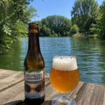 Poldergoud Tripel van Bospolder Brouwerij, fles en glas op een houten steiger aan groen water met bomen