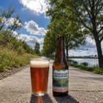 Sonnehoeck Grape Ale van Bospolder Brouwerij, glas en fles op een fietspad langs het water bij de Wollebrand in Honselersdijk