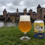 Grote Burgemeester Tripel van Seagull Brewing, glas en blik in het gras aan de gracht van een kasteel