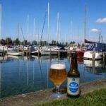 Rye of Sunshine van Gulden Triomfator, glas en fles op de kade van een jachthaven met zeilboten