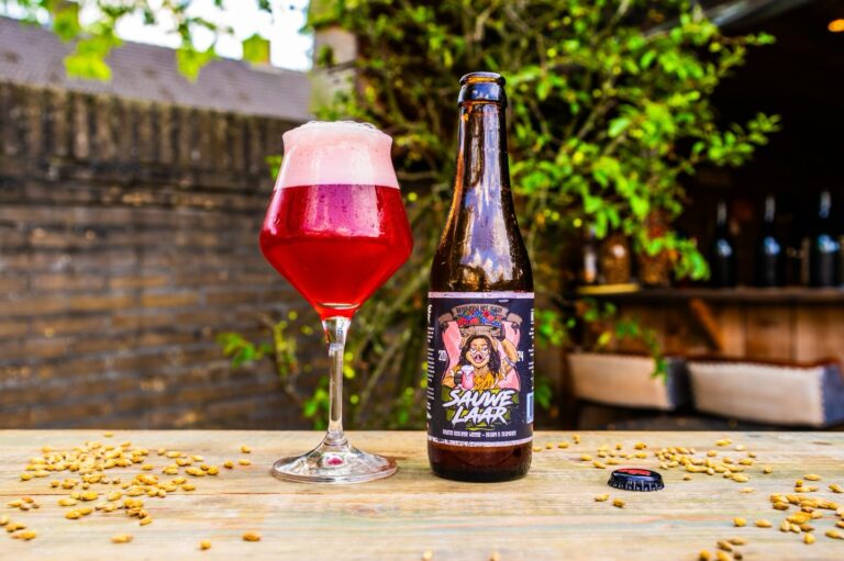 Sauwelaar Braam en Framboos van Het Zwijn, robijnrood glas en fles op een houten tafel met mout in een groene tuin