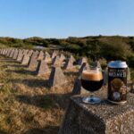 Malto Maple Madness van X-brewing, glas donkere stout en blik op een betonblok tussen de drakentanden in de duinen